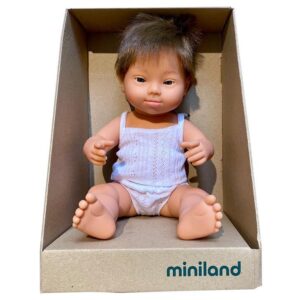 Boneco bebê menino loiro, branco, com síndrome de Down, com regata e shorts branco dentro da caixa  de papelão escrito miniland