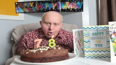 Homem idoso com sindrome de down apagando a sua vela de 78 anos, em um bolo de chocolate