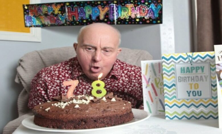Homem idoso com sindrome de down apagando a sua vela de 78 anos, em um bolo de chocolate