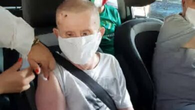 Idoso com síndrome de Down com máscara ele veste uma regata cinza, sentado no carro com cinto de segurança, tomando vacina