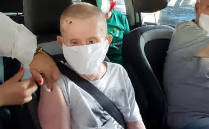 Idoso com síndrome de Down com máscara ele veste uma regata cinza, sentado no carro com cinto de segurança, tomando vacina