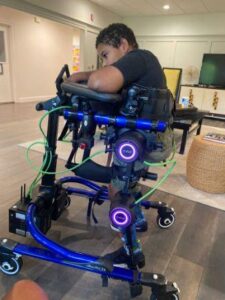 Menino branco com paralisia cerebral em cima de um equipamento roxo chamado exoesqueleto que o mantem em pé