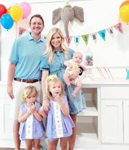 Na imagem aparece os pai usando camisa azul com suas filhas perto deles.