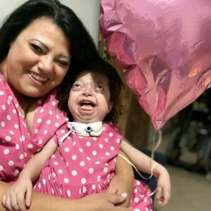 Mãe segura Manu no colo. As duas usam vestidinho rosa com bolinhas brancas.