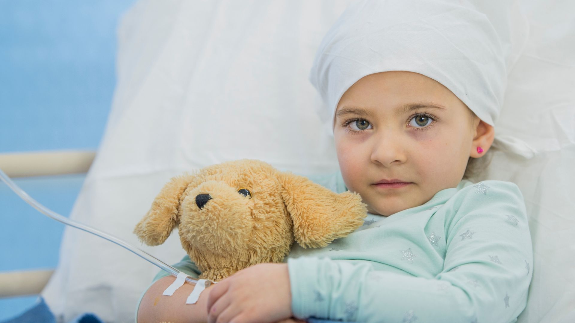 Menina deitada na cama de hospital com um urso aguardando a professora