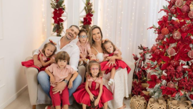 Família branca, sentada no sofá, pai, mãe e quintuplos, ao lado da árvore de natal