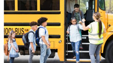 Imagem de um ônibus escolar, com crianças para embarcar, com um monitor de apoio