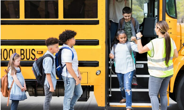 Imagem de um ônibus escolar, com crianças para embarcar, com um monitor de apoio