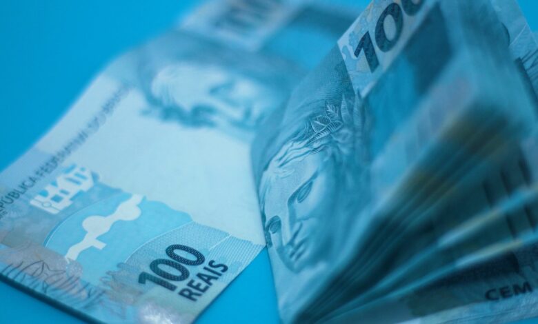 Imagem de fundo azul, com várias notas de 100 reais